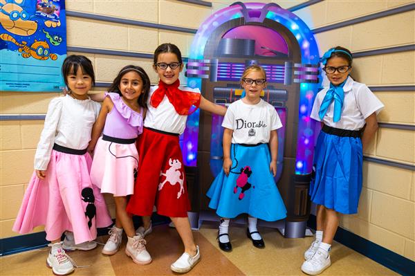 five girls in poodle skirts in front of a jukebox